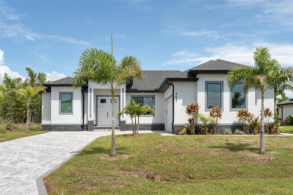 A modern single-story house with a white stucco facade, dark trim, and a paved driveway — 9487 ROSEBUD CIRCLE, PORT CHARLOTTE, FL