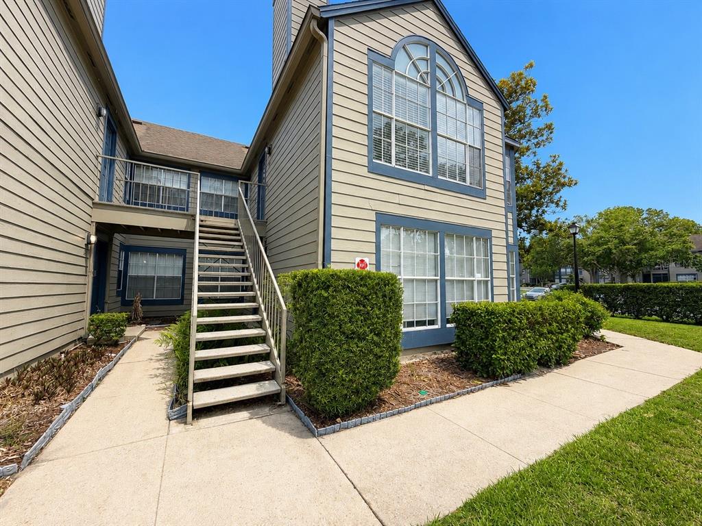 An exterior view of a two-story apartment building with beige siding and an outdoor staircase — 944 BAKEWELL COURT UNIT 106, LAKE MARY, FL