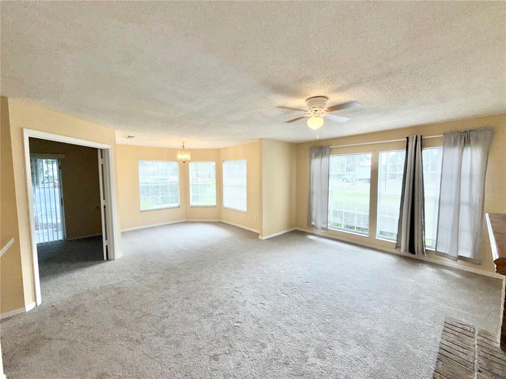 A spacious living room features beige carpet, tan walls, large windows, and a ceiling fan — 944 BAKEWELL COURT UNIT 106, LAKE MARY, FL