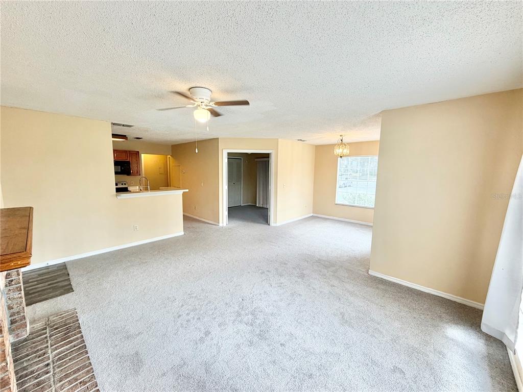 A living room with beige carpet, a ceiling fan, and an open kitchen area — 944 BAKEWELL COURT UNIT 106, LAKE MARY, FL