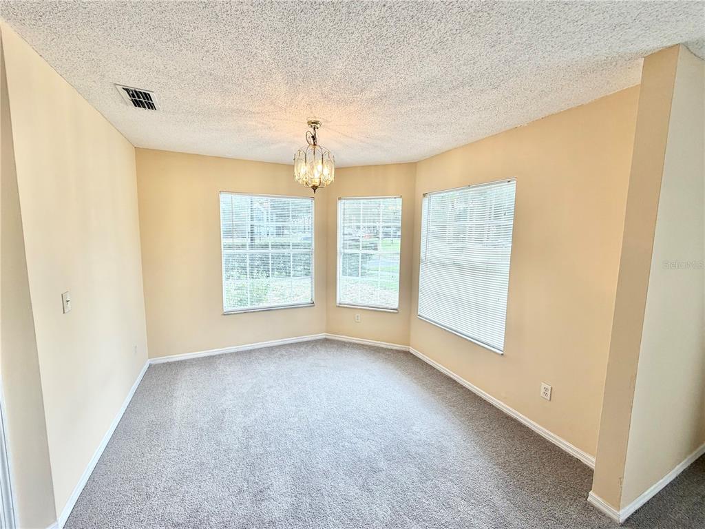 An empty dining area features beige walls, gray carpeting, and a central chandelier — 944 BAKEWELL COURT UNIT 106, LAKE MARY, FL