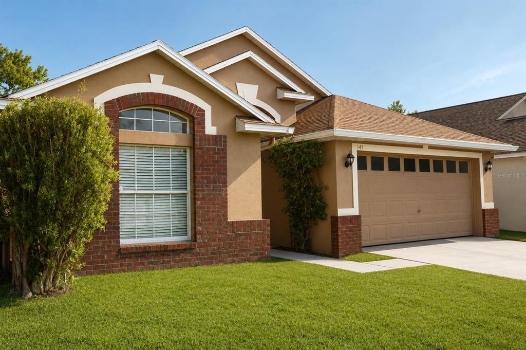 A single-story house with a tan stucco exterior, brick accents, and a two-car garage — 145 THORNBURY DRIVE, KISSIMMEE, FL