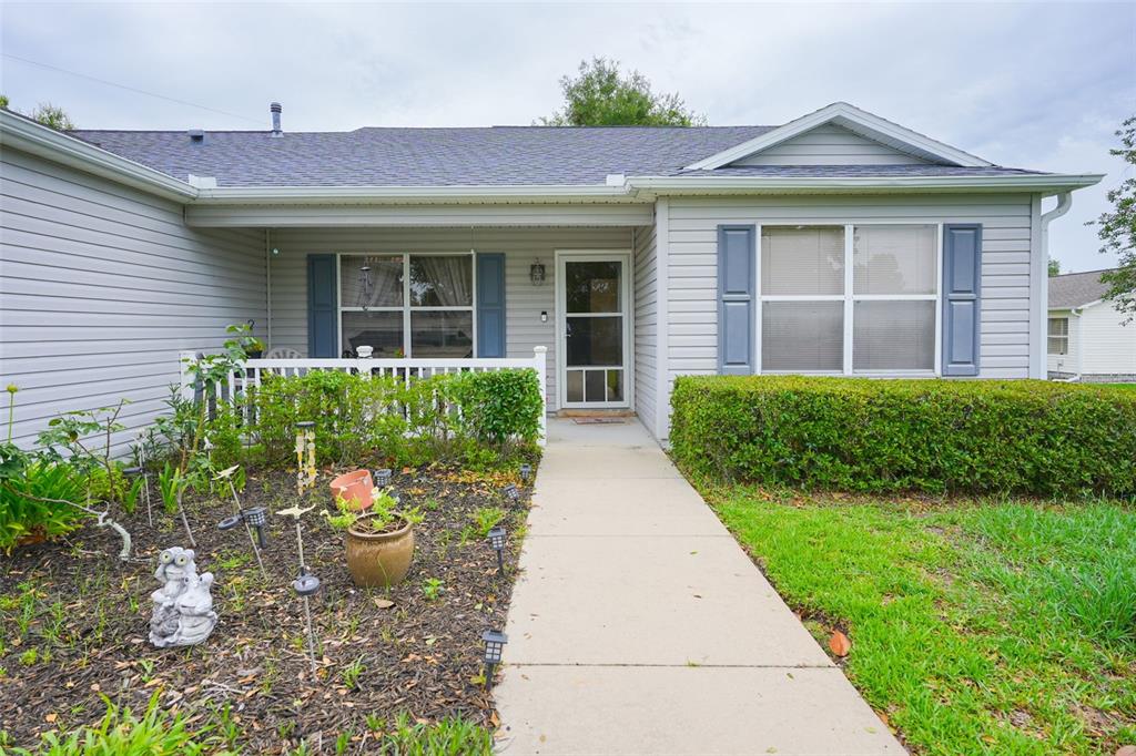 A single-story house with light gray siding, blue shutters, and a concrete walkway to the entrance — 9345 SE 177TH SIMONS LANE, THE VILLAGES, FL