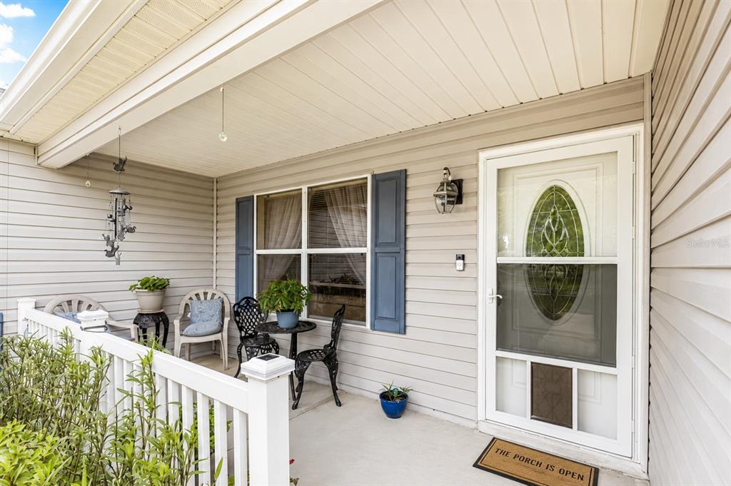 A covered front porch with light gray siding, a white railing, and a glass-paneled door — 9345 SE 177TH SIMONS LANE, THE VILLAGES, FL