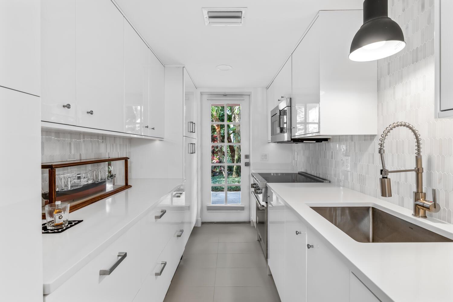 A narrow galley kitchen features white high-gloss cabinets, quartz countertops, and a glass-paned exterior door — 134 Peruvian Avenue # 104, Palm Beach FL 33480, PALM BEACH, FL