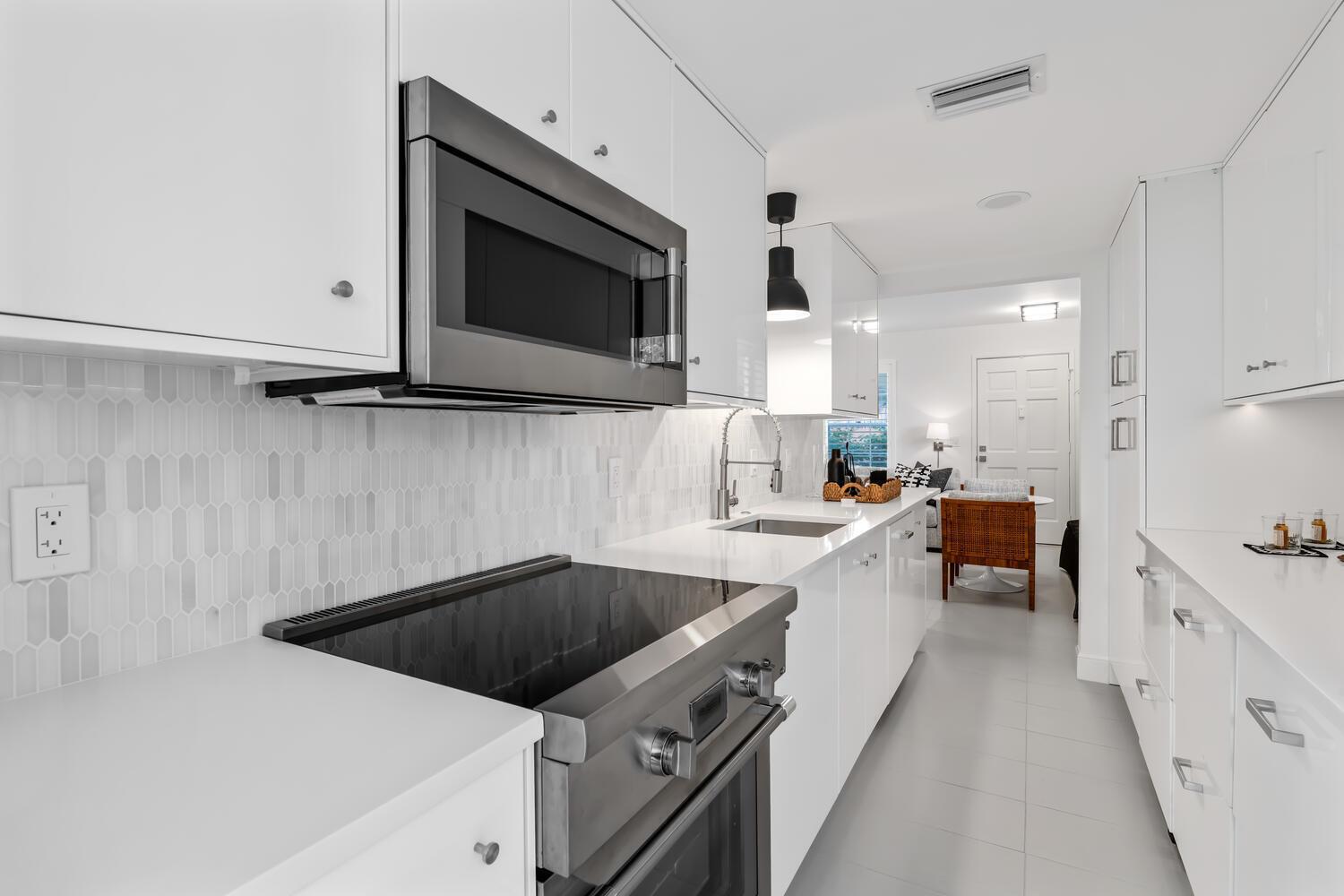 A modern white kitchen features stainless steel appliances, a tiled backsplash, and light-colored countertops — 134 Peruvian Avenue # 104, Palm Beach FL 33480, PALM BEACH, FL