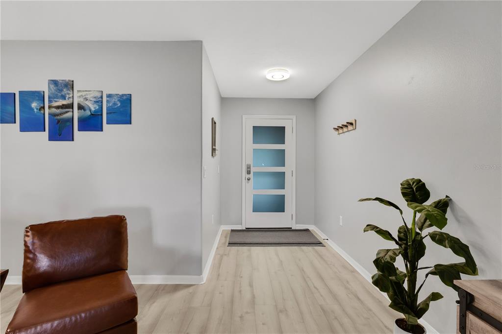 An entryway features light wood flooring, a white front door with glass panels, and wall art — 2757 FEIFFER CIRCLE, SARASOTA, FL