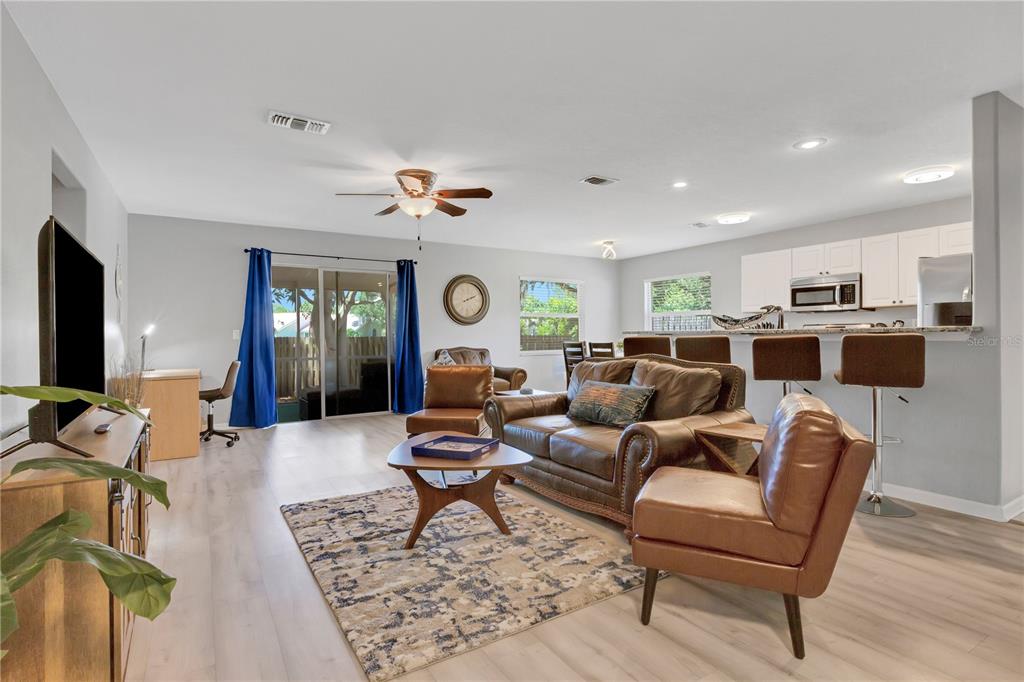 An open-concept living room and kitchen featuring wood-look flooring, leather furniture, and a sliding door — 2757 FEIFFER CIRCLE, SARASOTA, FL