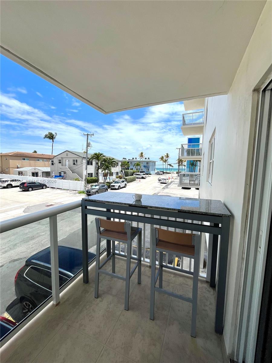 A balcony features a high-top granite table with two chairs overlooking a street and ocean — 1801 S Ocean Dr # 203, Hollywood FL 33019, HOLLYWOOD, FL