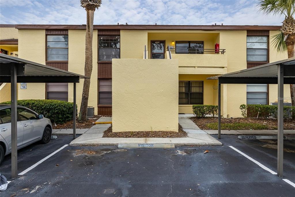 A yellow exterior wall features a front door, a window, and a red fire alarm — 13608 S VILLAGE DRIVE UNIT 7204, TAMPA, FL
