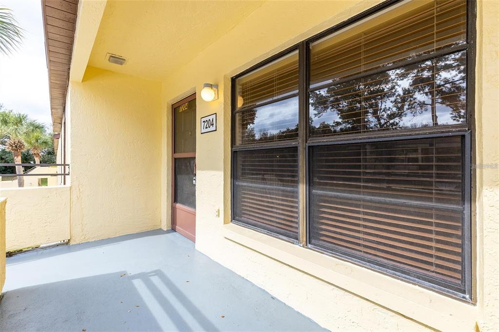 A yellow exterior wall features a front door and a large window with blinds — 13608 S VILLAGE DRIVE UNIT 7204, TAMPA, FL