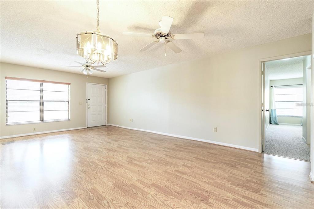 A living room with wood-look flooring, a ceiling fan, a chandelier, and a doorway — 13608 S VILLAGE DRIVE UNIT 7204, TAMPA, FL