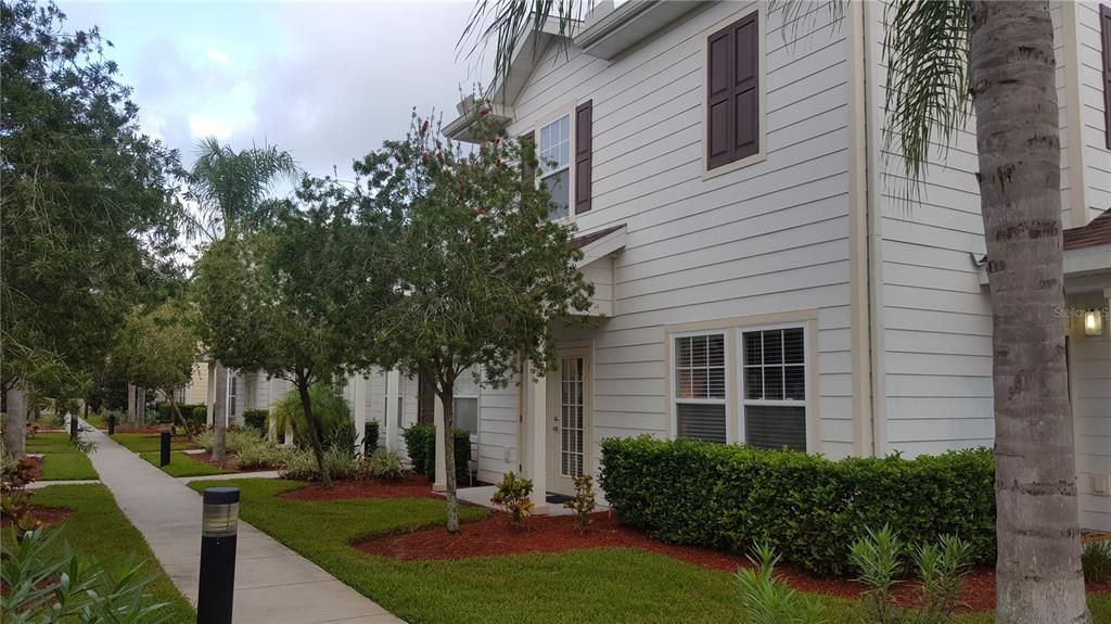 A two-story white house with dark shutters sits beside a sidewalk and landscaped lawn — 5362 DIPLOMAT COURT UNIT 108, KISSIMMEE, FL