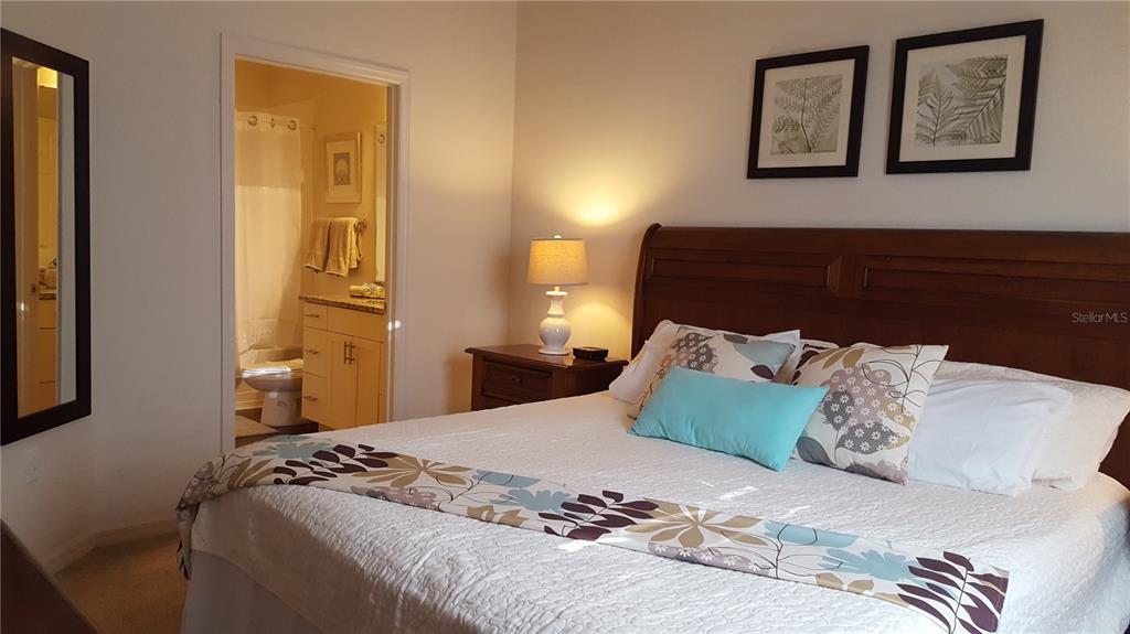 A bedroom features a wooden headboard, a patterned bed runner, and an attached bathroom — 5362 DIPLOMAT COURT UNIT 108, KISSIMMEE, FL