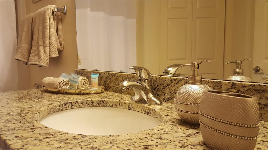 A bathroom vanity features a granite countertop, a chrome faucet, and matching decorative accessories — 5362 DIPLOMAT COURT UNIT 108, KISSIMMEE, FL