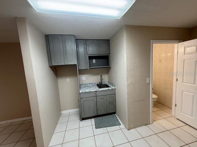 A small kitchenette with gray cabinets, a sink, and tiled flooring sits beside a bathroom — 15 UTILITY DRIVE UNIT C, PALM COAST, FL