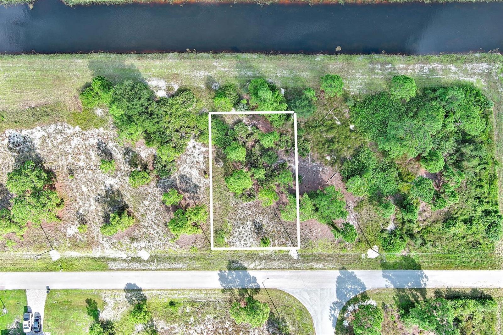 An aerial view shows a rectangular plot of land with trees and vegetation near a canal — 745 Troy Ave, Lehigh Acres FL 33974, LEHIGH ACRES, FL