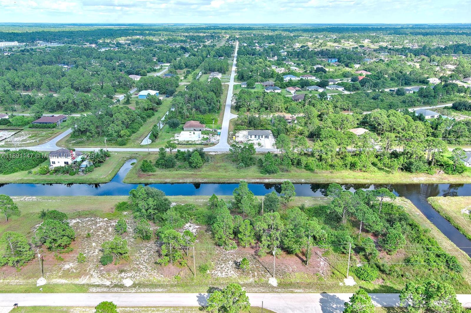 An aerial view shows a vacant lot with trees and brush bordering a canal — 745 Troy Ave, Lehigh Acres FL 33974, LEHIGH ACRES, FL