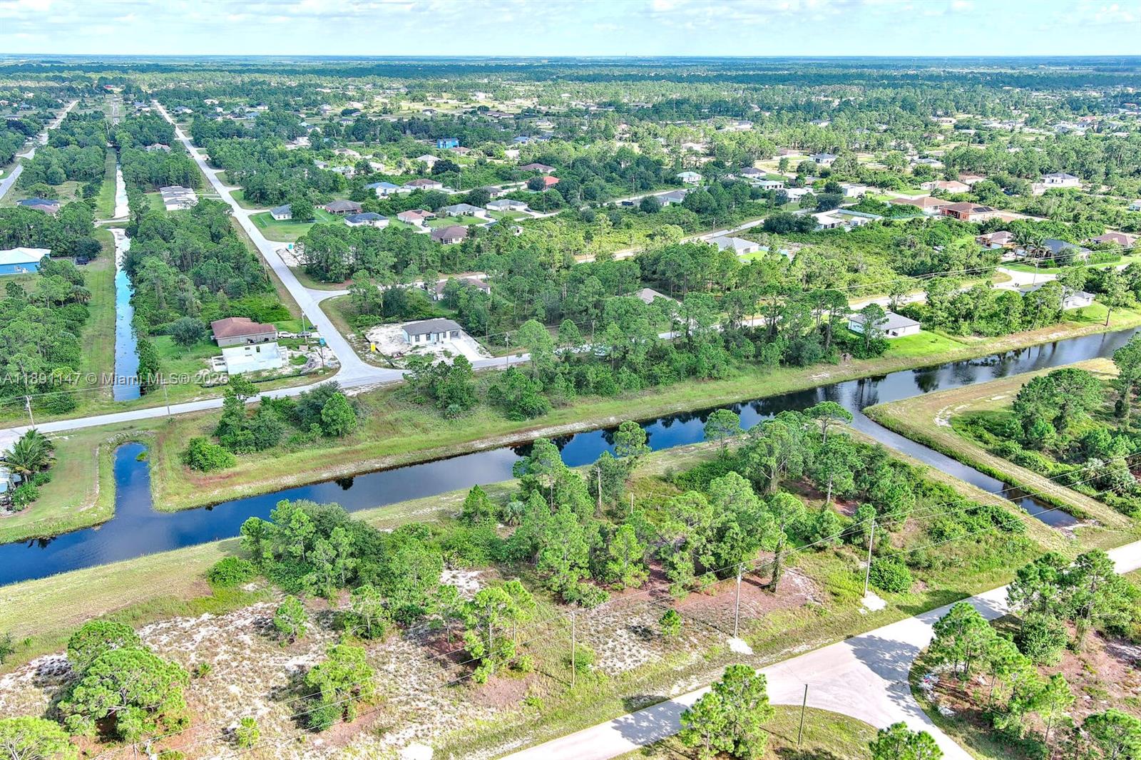 An aerial view shows a residential area with scattered houses, dense vegetation, and intersecting canals — 745 Troy Ave, Lehigh Acres FL 33974, LEHIGH ACRES, FL