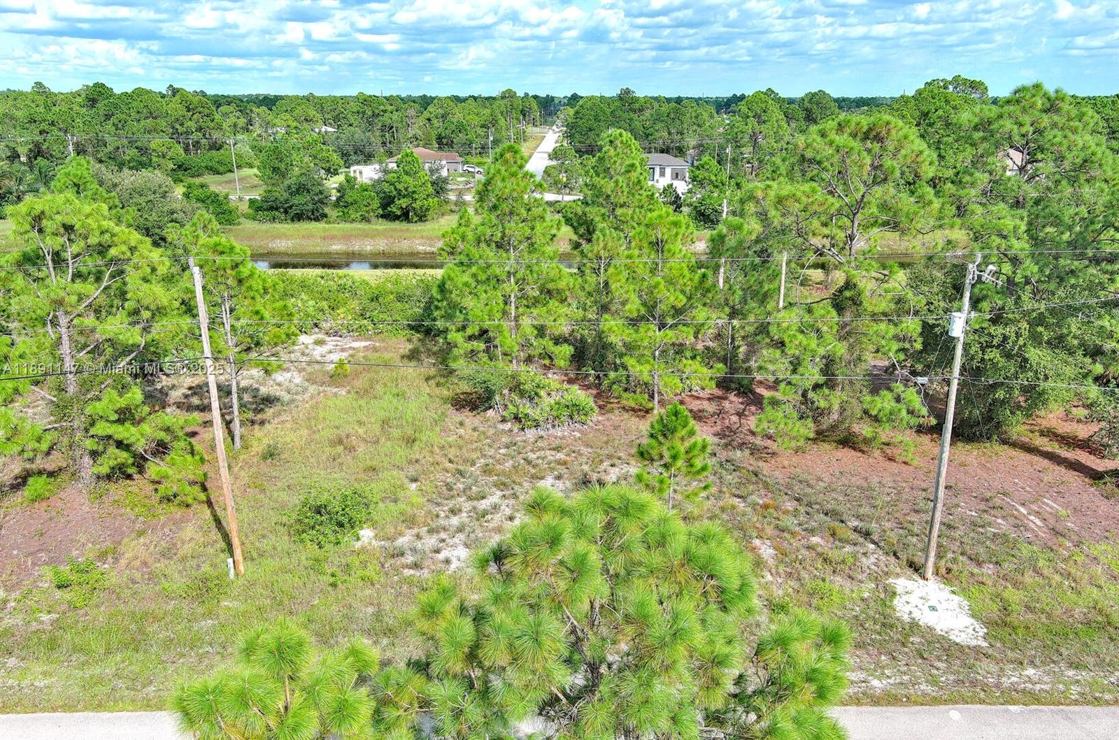 An aerial view shows a vacant, wooded lot with a canal and distant houses — 745 Troy Ave, Lehigh Acres FL 33974, LEHIGH ACRES, FL