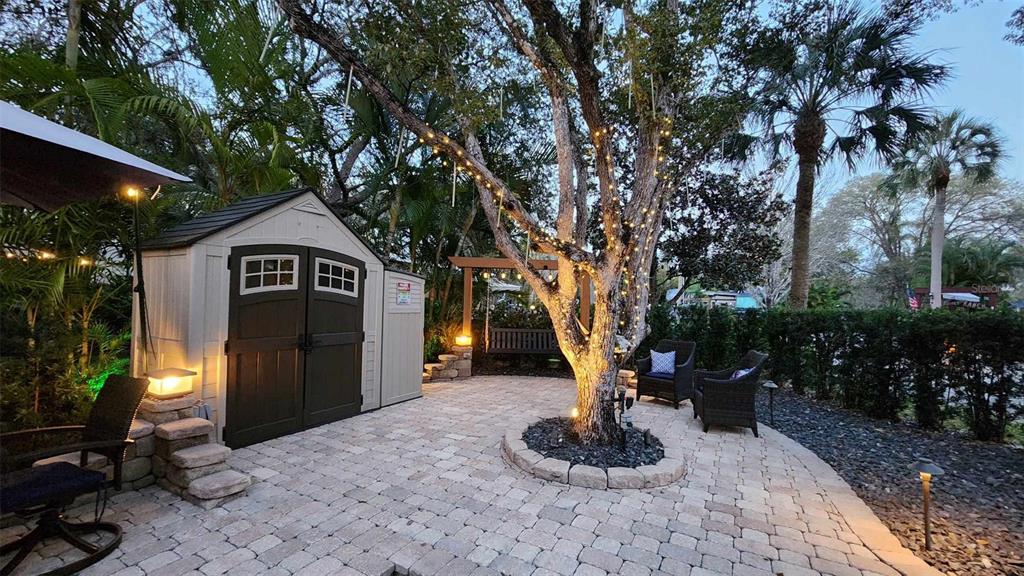 A paved patio features a storage shed, a lighted tree, and outdoor seating at dusk — 140 APPALOOSA TRAIL, RIVER RANCH, FL