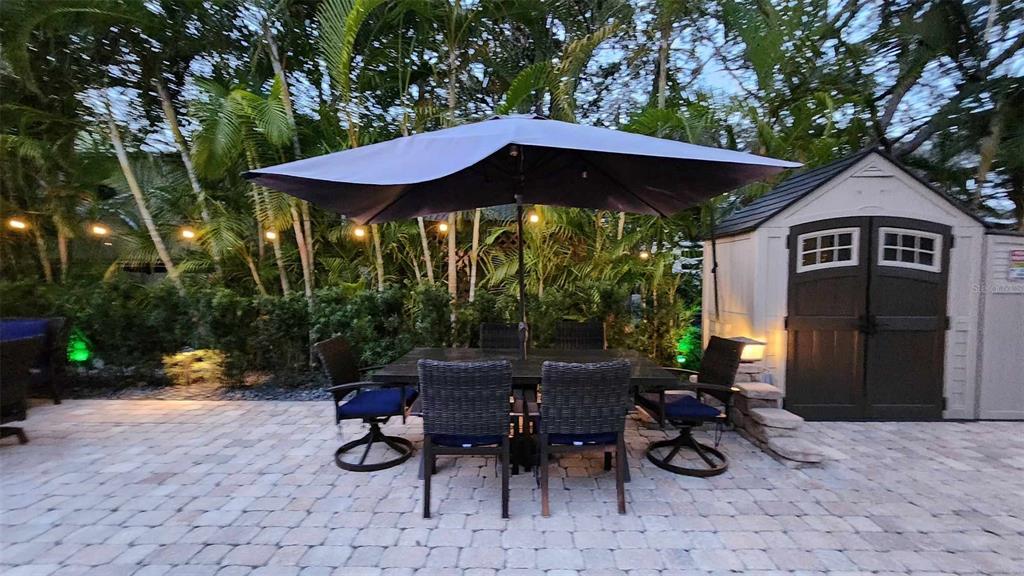 A patio features a dining set with an umbrella, string lights, and a storage shed — 140 APPALOOSA TRAIL, RIVER RANCH, FL