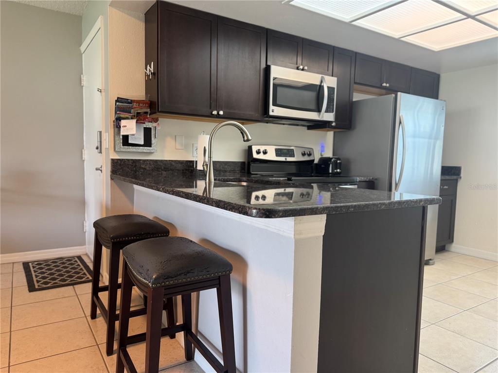 A kitchen features dark wood cabinets, granite countertops, a breakfast bar with stools, and appliances — 115 WINDWARD PLACE UNIT 15, OLDSMAR, FL