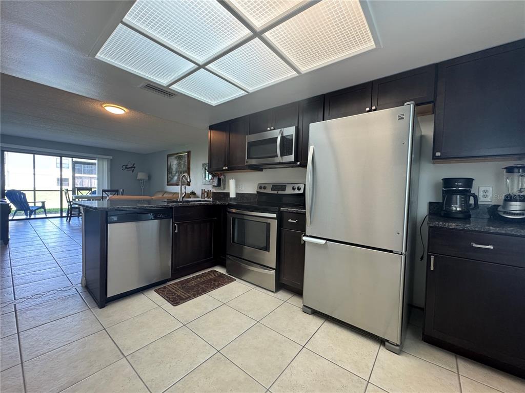 A kitchen features dark wood cabinets, stainless steel appliances, and light-colored tile flooring — 115 WINDWARD PLACE UNIT 15, OLDSMAR, FL