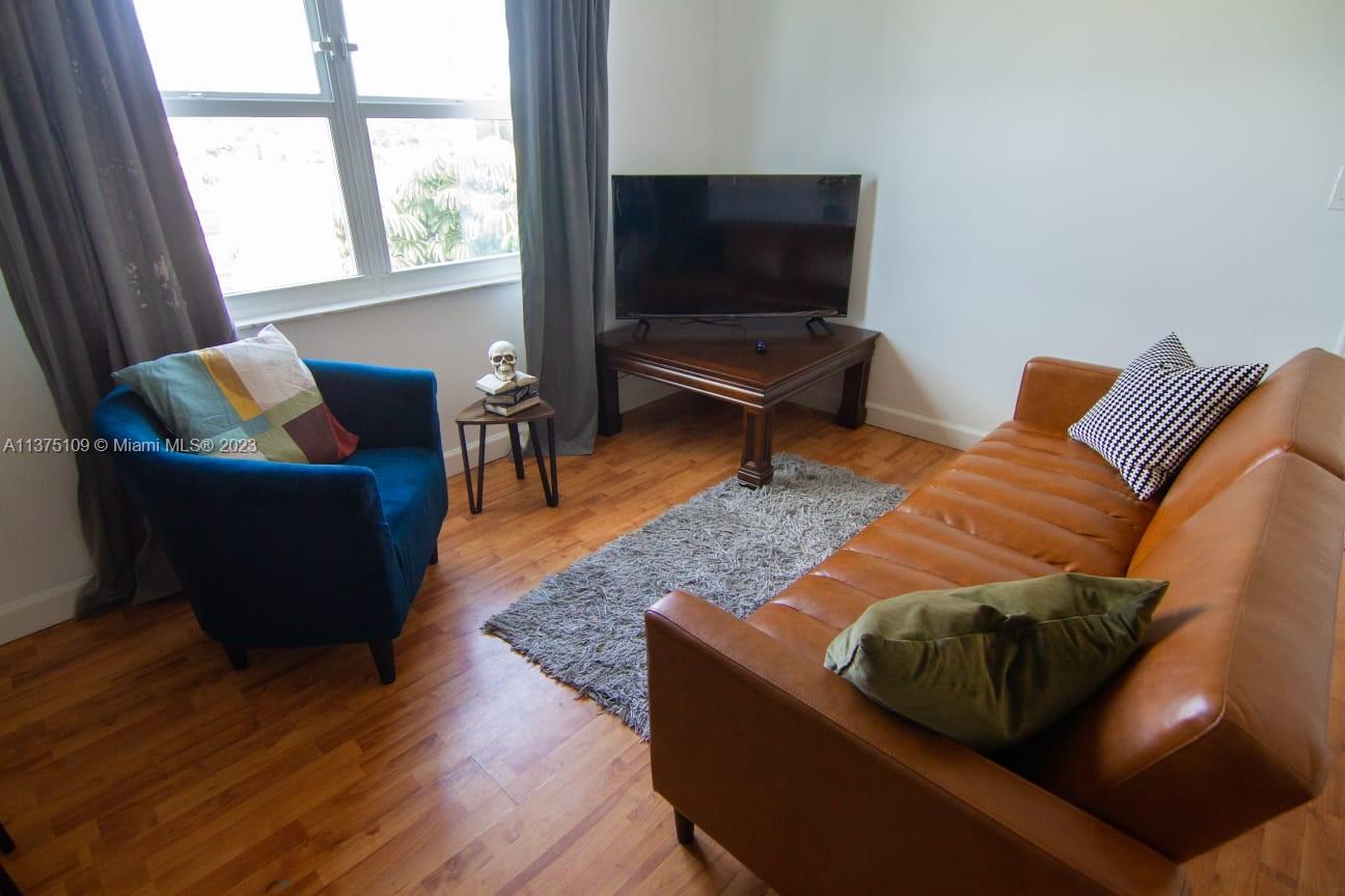 A living room features a brown leather sofa, a blue armchair, and a corner television stand — 753 Michigan Ave # 3D, Miami Beach FL 33139, MIAMI BEACH, FL