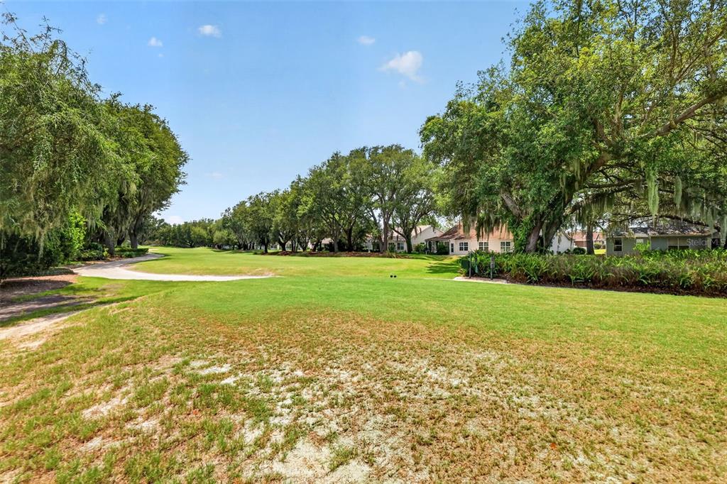 A grassy golf course fairway is bordered by large oak trees and residential houses — 542 LOMA PASEO DRIVE, THE VILLAGES, FL