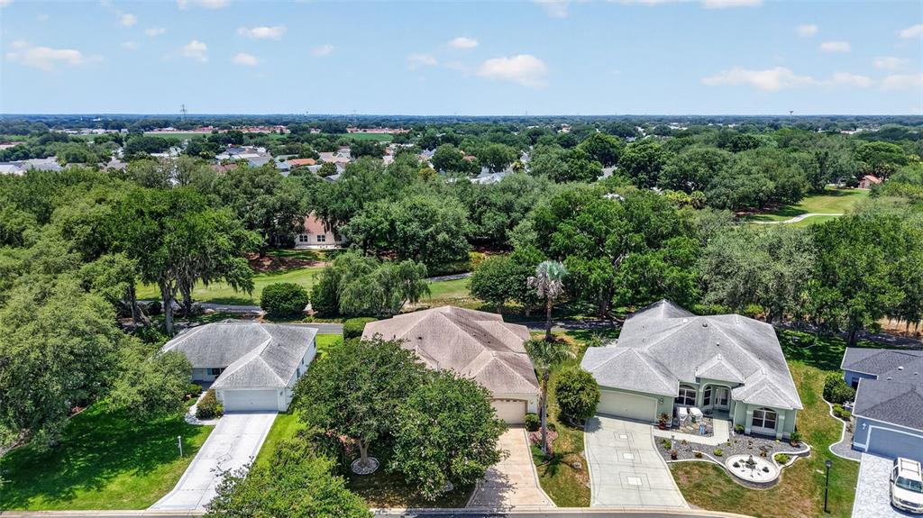 An aerial view shows three suburban houses with driveways surrounded by lush green trees — 542 LOMA PASEO DRIVE, THE VILLAGES, FL