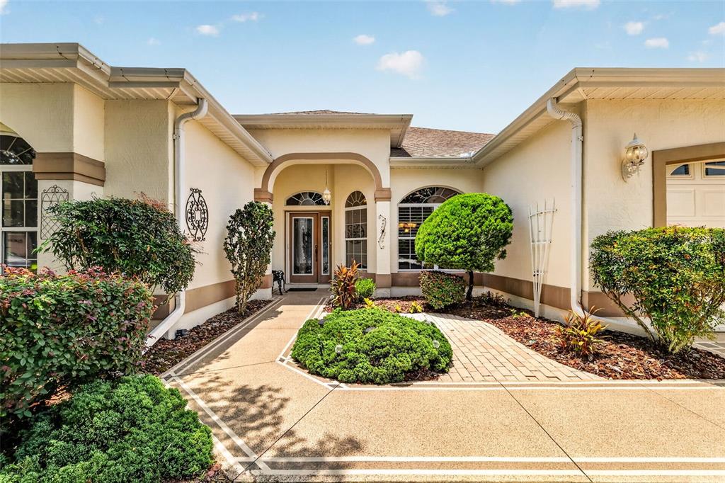 The exterior of a beige house features a paved walkway leading to a recessed front entrance — 542 LOMA PASEO DRIVE, THE VILLAGES, FL