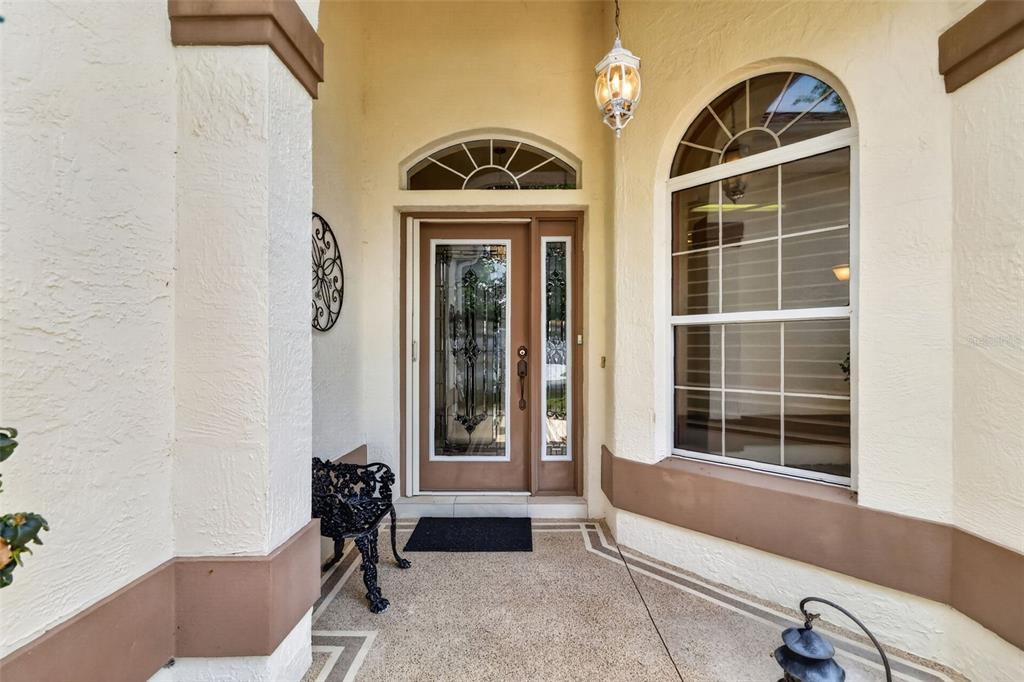 A covered entryway features a glass-paneled front door, a large arched window, and textured walls — 542 LOMA PASEO DRIVE, THE VILLAGES, FL