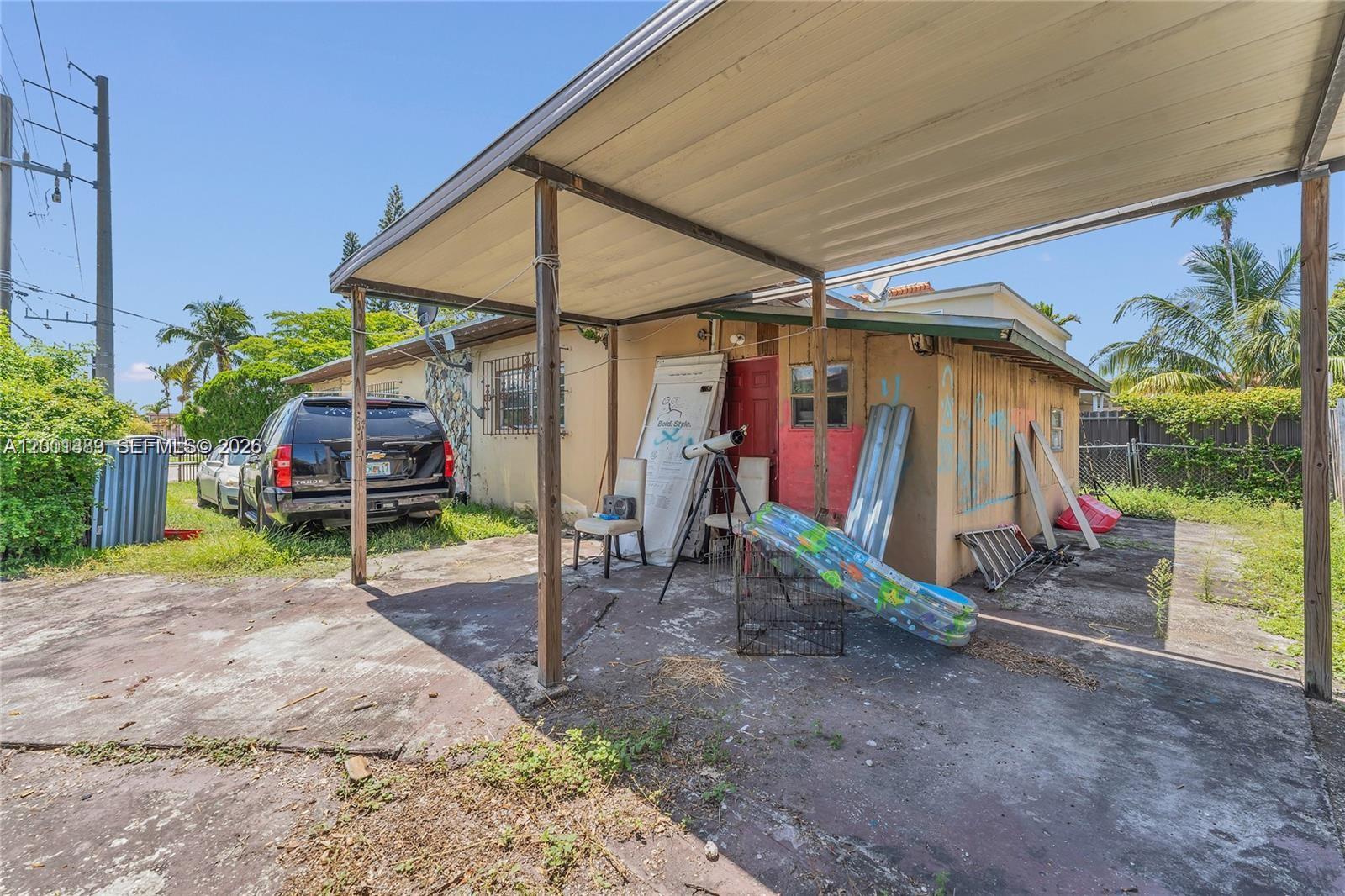 A carport covers a concrete driveway in front of a house with a red door — 503 NW 43rd Pl, Miami FL 33126, MIAMI, FL