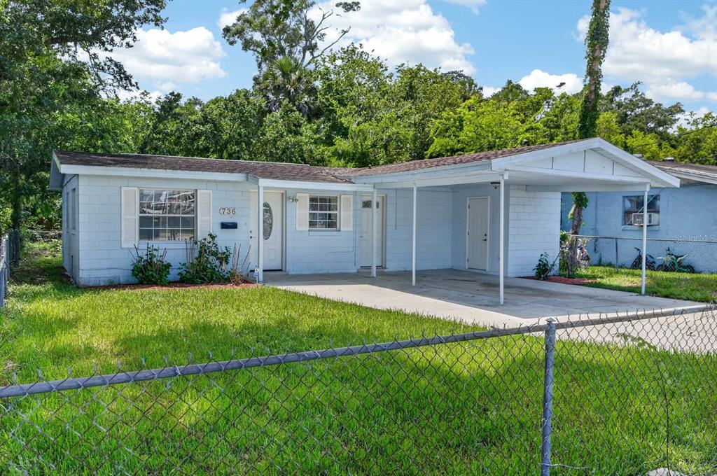 A light blue, single-story house with a carport and a chain-link fence in the yard — 736 S CAROLINE STREET, DAYTONA BEACH, FL