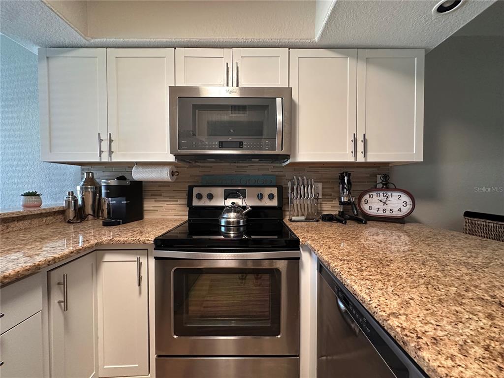 A kitchen features white cabinets, stainless steel appliances, and speckled granite countertops — 4923 25TH STREET W UNIT 104, BRADENTON, FL