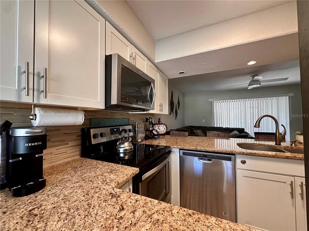 A kitchen features granite countertops, white cabinets, stainless steel appliances, and a tile backsplash — 4923 25TH STREET W UNIT 104, BRADENTON, FL