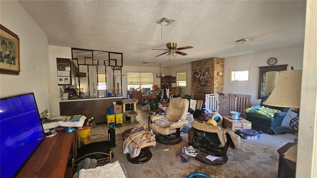 A living room with a brick fireplace, carpeted floors, and a kitchen pass-through window — 43734 WEST LANE, PAISLEY, FL