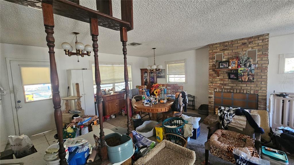 A cluttered dining and living area features a brick fireplace, wooden room divider, and chandelier — 43734 WEST LANE, PAISLEY, FL