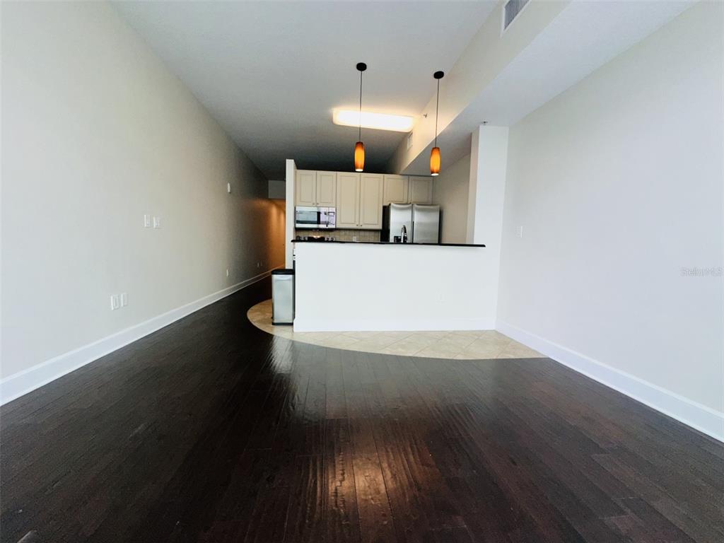 A kitchen with white cabinets and stainless steel appliances overlooks a dark wood-floored living area — 101 S EOLA DRIVE UNIT 518, ORLANDO, FL