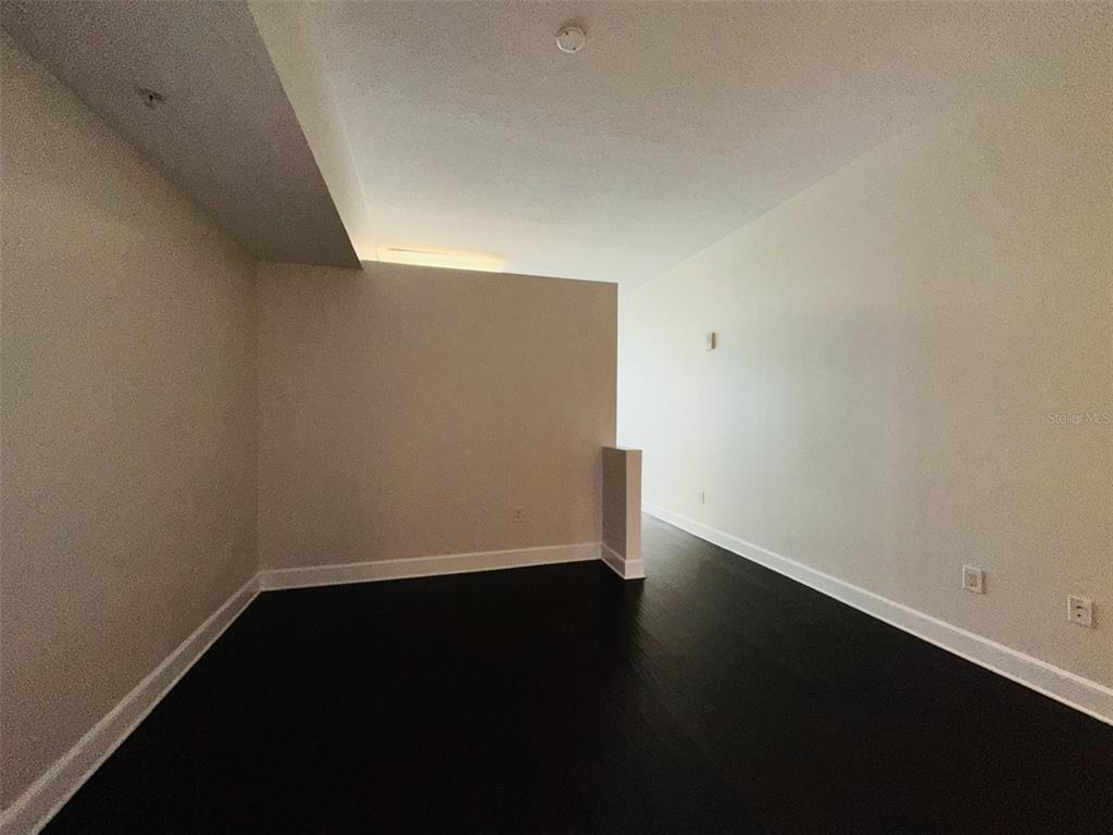 An empty room with dark wood flooring, white walls, and a partial partition wall — 101 S EOLA DRIVE UNIT 518, ORLANDO, FL