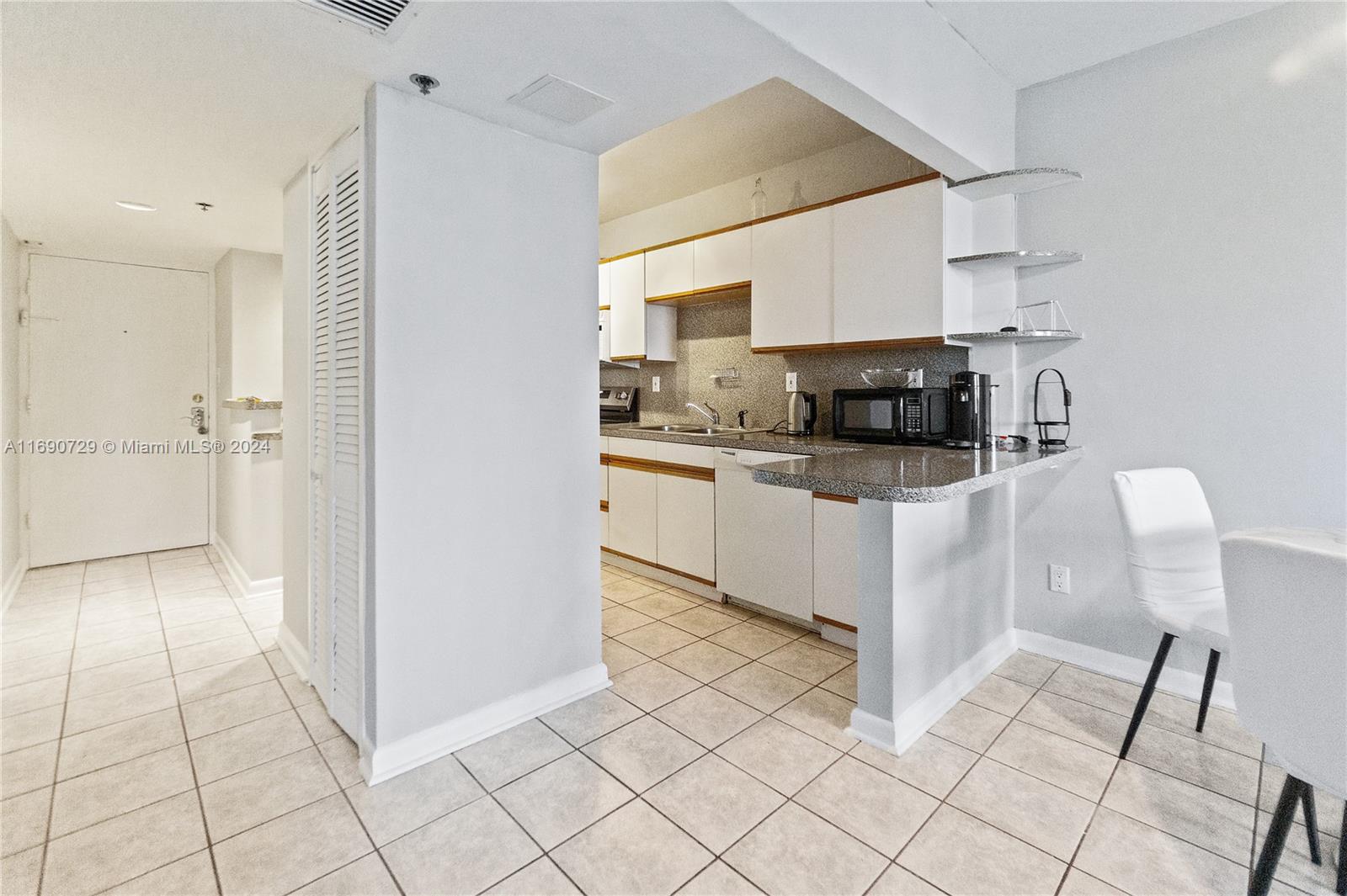 A kitchen with white cabinets, granite countertops, and tile flooring opens to a dining area — 100 Lincoln Rd # 1019, Miami Beach FL 33139, MIAMI BEACH, FL