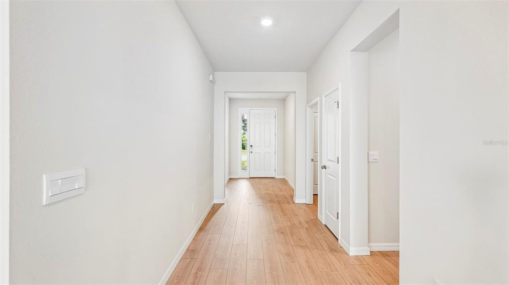 A bright hallway features light wood-look flooring, white walls, and a white front door — 2814 FISHERY COURT, LAKEWOOD RANCH, FL