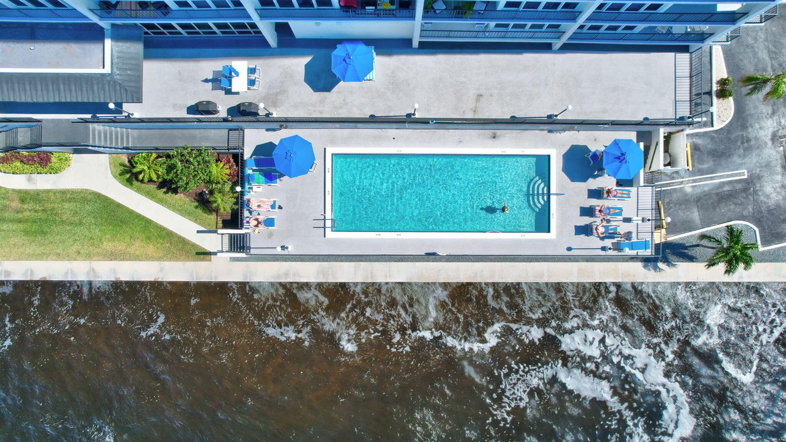 An aerial view shows a rectangular swimming pool with lounge chairs beside a waterfront building — 521 N Riverside Drive # 1207, Pompano Beach FL 33062, POMPANO BEACH, FL