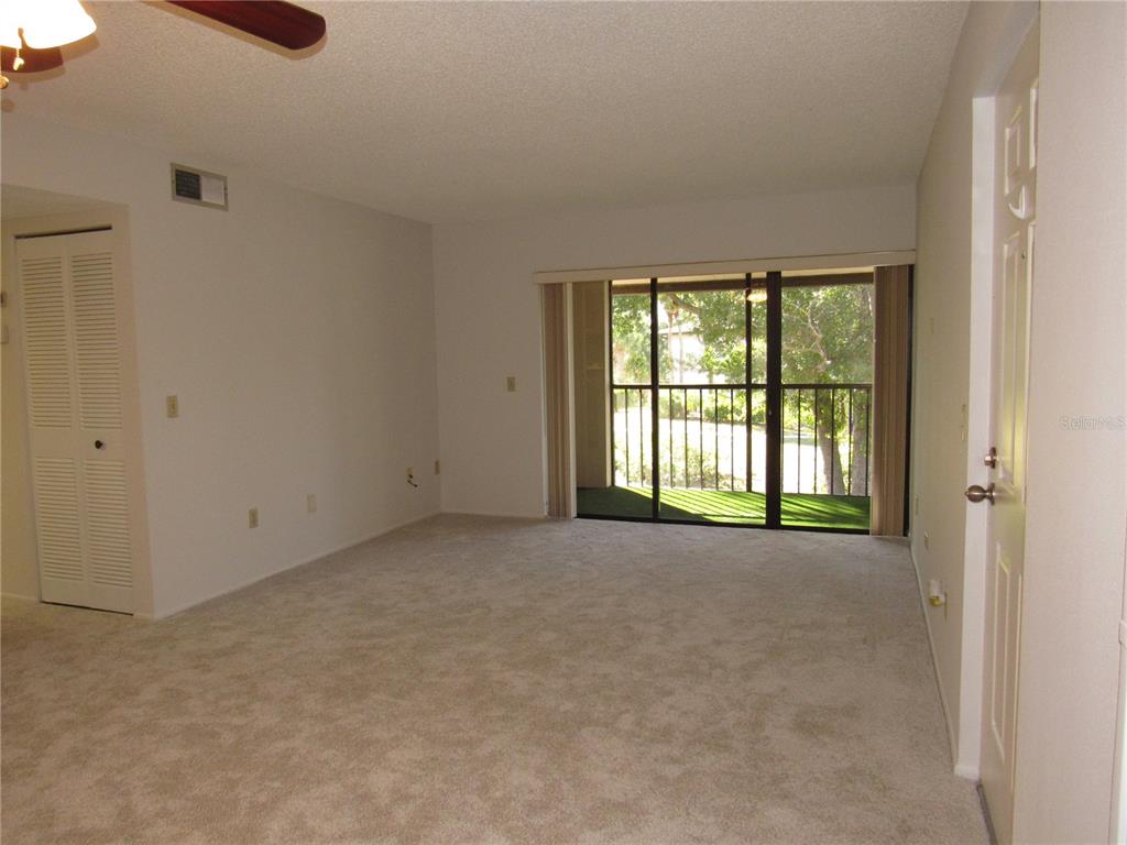 An empty living room features beige carpeting, white walls, a ceiling fan, and sliding glass doors — 1515 FORREST NELSON BOULEVARD UNIT N201, PORT CHARLOTTE, FL