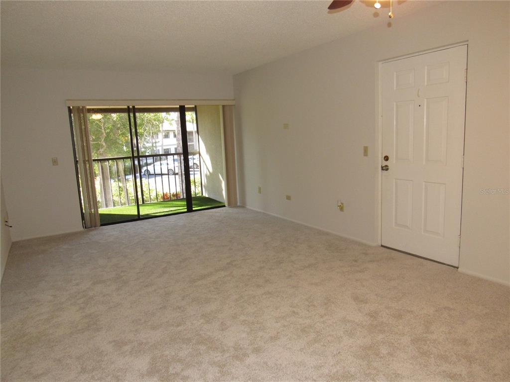 An empty living room features beige carpeting, white walls, a sliding glass door, and an entrance — 1515 FORREST NELSON BOULEVARD UNIT N201, PORT CHARLOTTE, FL