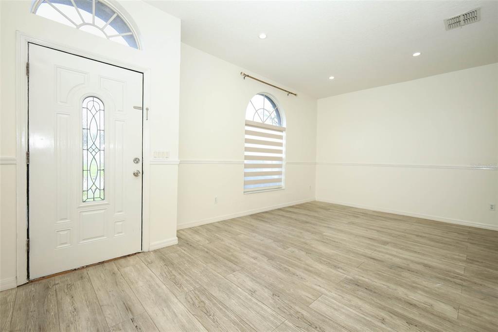 An empty room with light wood-look flooring, white walls, a front door, and arched windows — 9345 MONTEREY BAY DRIVE, ORLANDO, FL