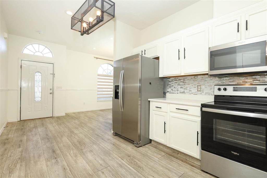 A kitchen with white cabinets, stainless steel appliances, and wood-look flooring next to an entryway — 9345 MONTEREY BAY DRIVE, ORLANDO, FL
