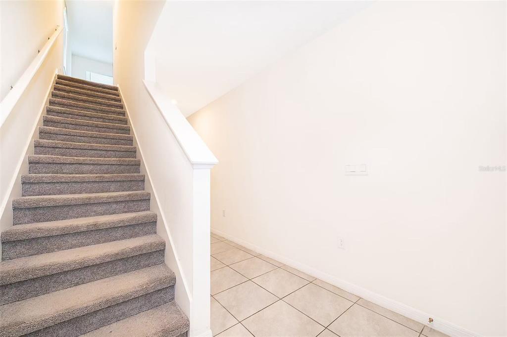 A carpeted staircase sits beside a console table with a lamp and floral arrangement — 30915 PENNY SURF LOOP, WESLEY CHAPEL, FL