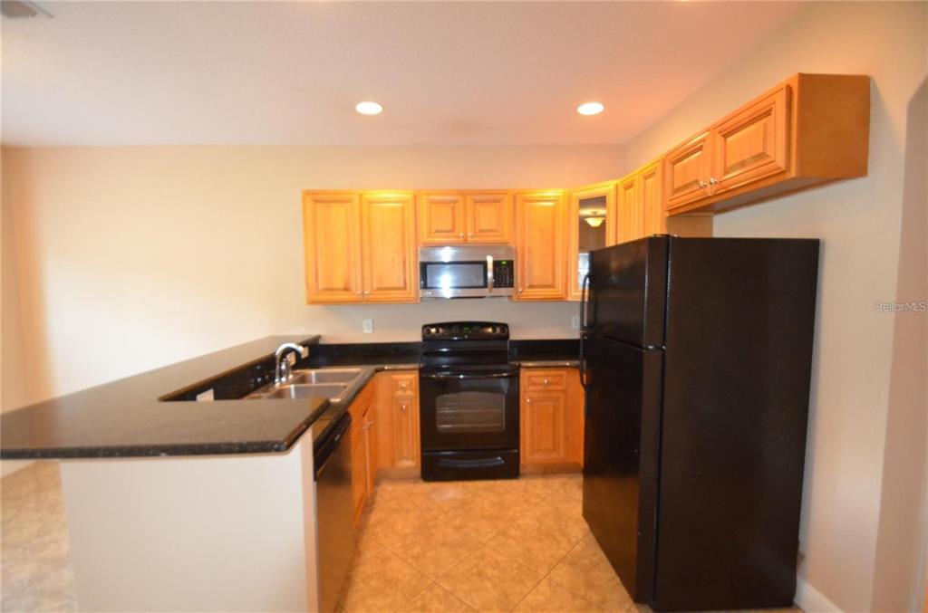 A kitchen features light wood cabinets, black countertops, black appliances, and tile flooring — 3725 S LAKE ORLANDO PKWY UNIT 1, ORLANDO, FL